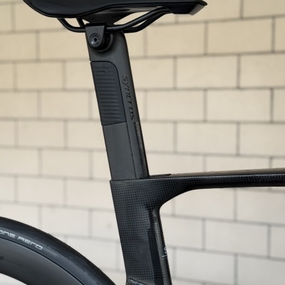 Sela de bicicleta preta com canote e quadro preto carbono, pneu Continental Grand Prix 5000, parede tijolos brancos atrás