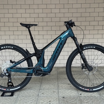 Bicicleta de montanha elétrica SCOTT azul e preta contra parede de azulejos cinzas