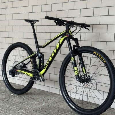 Bicicleta de montanha Scott preta com detalhes amarelo-fluorescente perto de parede de azulejos brancos