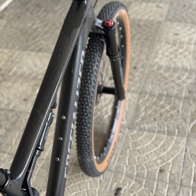 Bicicleta preta de montanha com pneus castanhos e suspensão dianteira em piso de calçada