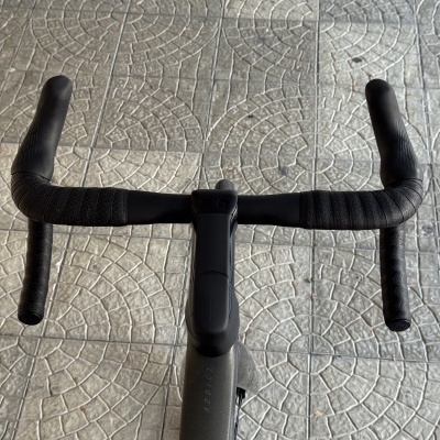 Guiador de bicicleta de estrada preto com fita preta e manípulos pretos, em piso de pedra com padrão circular