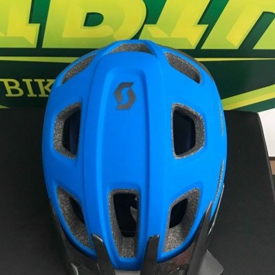 Capacete de bicicleta azul com detalhes em preto sobre superfície preta e fundo verde-amarelo