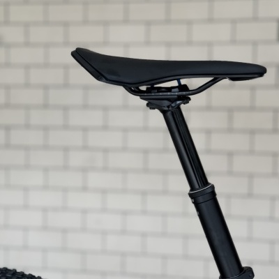 Selim preto de bicicleta com pneu grosso e parede de tijolos branca ao fundo