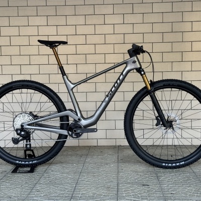 Bicicleta de montanha Scott cinza metálico com detalhes dourados e pneus Maxxis