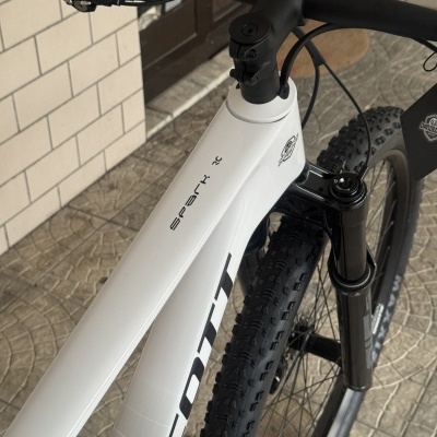 Bicicleta de montanha branca com detalhes a preto num espaço interior com chão e parede de azulejos
