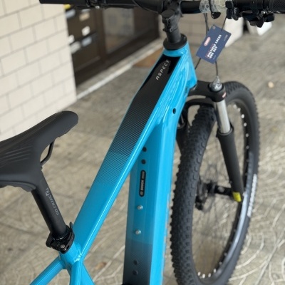 Bicicleta elétrica azul e preta apoiada num piso de pedra com etiqueta no guiador