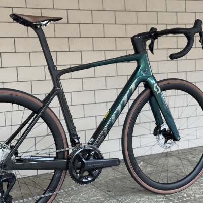 Bicicleta de estrada carbono verde escuro com rodas pneus castanhos num piso de azulejos