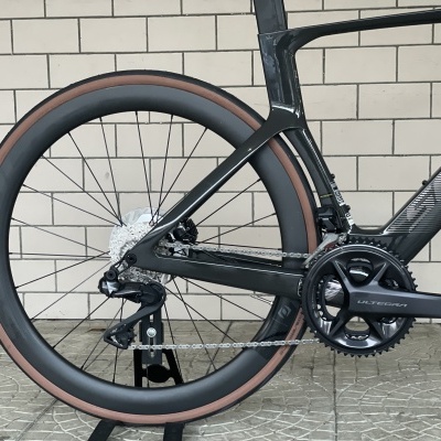 Parte traseira de bicicleta de corrida preta em carbono com pneu marron, pedaleira Shimano Ultegra.