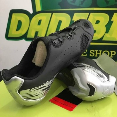 Sapatos de ciclismo preto e prateado com logótipo S3 e fundo verde de loja