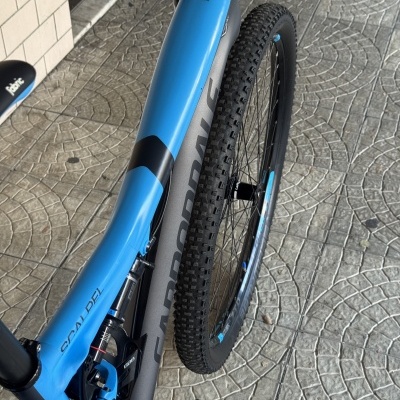 Bicicleta de montanha azul e cinza Cannondale com roda e pneu preto, selim preto com texto branco, em pavimento cinzento