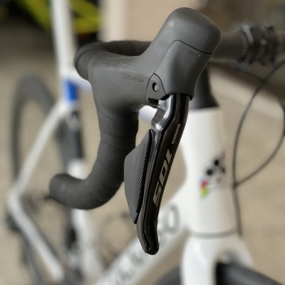 Bicicleta branca de estrada com guiador preto e alavanca Shimano 105