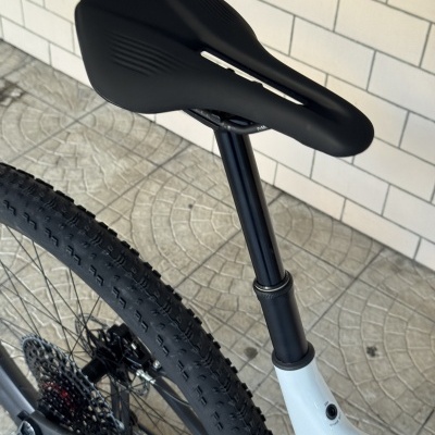 Selim preto de bicicleta com canote e roda traseira perto de parede branca azulejada