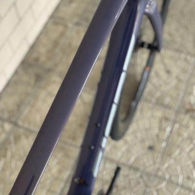Bicicleta azul com texto DEFY encostada a parede branca e piso de pedra