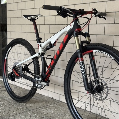 Bicicleta de montanha com quadro branco e preto e detalhes vermelhos encostada numa parede de azulejos brancos