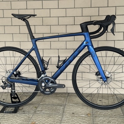 Bicicleta de estrada azul metálico apoiada num suporte junto a uma parede de tijolos