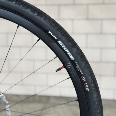 Pneu de bicicleta Maxxis Receptor preto montado numa roda com parede branca ao fundo