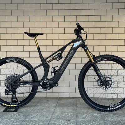 Bicicleta de montanha Cannondale preta com suspensão dourada encostada na parede.