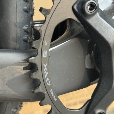 Prato de bicicleta preto Shimano GRX 12S 40T junto a pneu preto com relevos