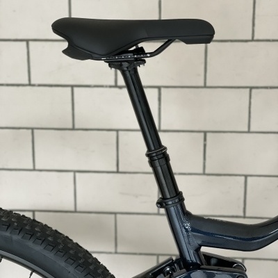 Assento de bicicleta preto com tubo e quadro azul escuro contra parede branca de azulejos