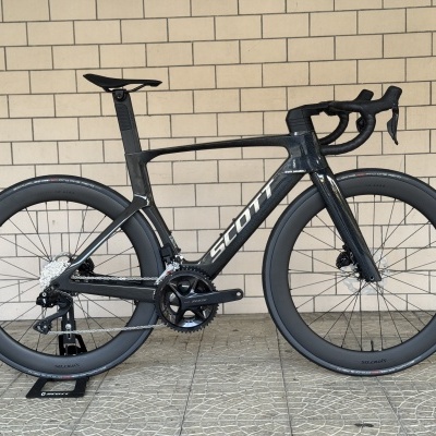 Bicicleta de estrada SCOTT em fibra de carbono preta numa parede de tijolos.