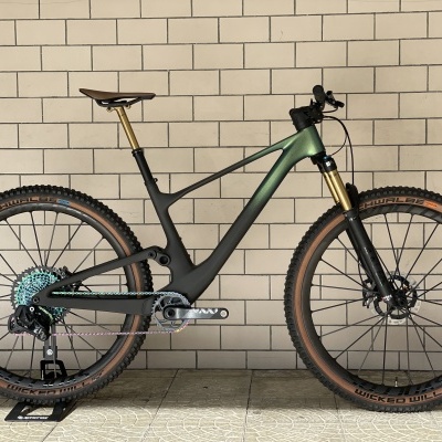 Bicicleta de montanha carbono preta e verde com pneus pretos e castanhos junto a parede de azulejos brancos