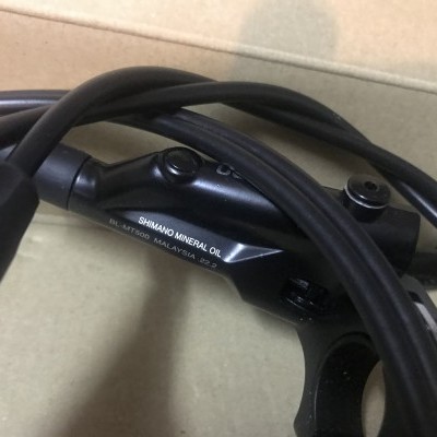 Freio hidráulico para bicicleta preto com cabos enrolados numa caixa de cartão