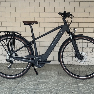 Bicicleta elétrica preta com selim castanho e acessórios, encostada numa parede de tijolos