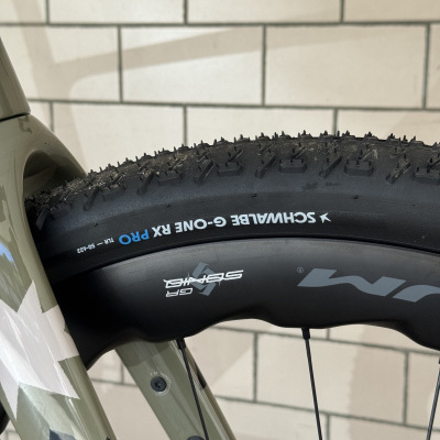 Pneu de bicicleta preto cravado com texto SCHWALBE G-ONE RX PRO montado em aro preto e quadro bege com detalhes camuflados