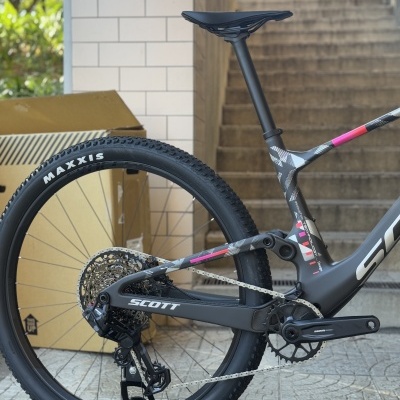 Bicicleta de montanha SCOTT com roda traseira MAXXIS, quadro preto e detalhes rosa, em ambiente exterior junto a escadas