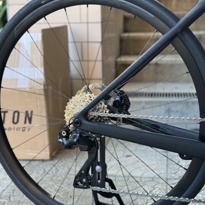 Roda traseira de bicicleta com pneu preto e cassete dourada junto a caixas e escadas.