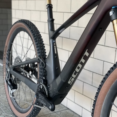 Bicicleta de montanha SCOTT preta com pneus castanhos e suspensão dourada encostada numa parede