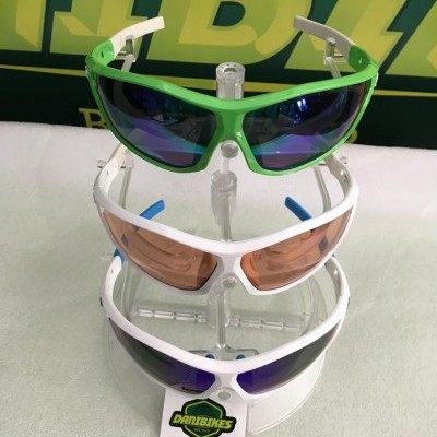 Três óculos de sol desportivos empilhados com armações verde e branca e lentes espelhadas em suporte transparente