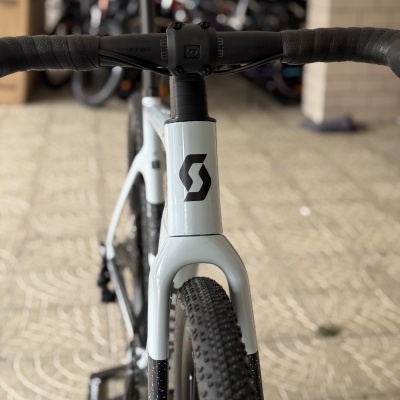 Uma bicicleta branca com pneus pretos e guiador preto em primeiro plano.