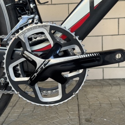 Pedaleira com prato de bicicleta preto e prateado com texto Full Speed Ahead em ambiente com pavimento e parede de tijolos
