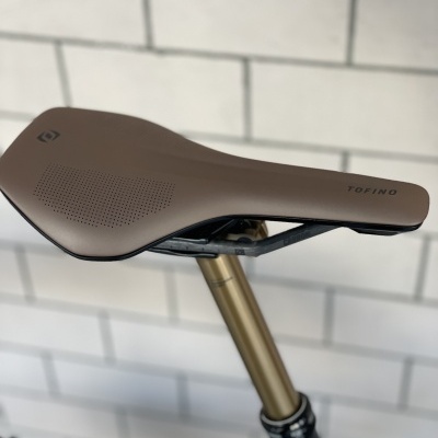 Selim de bicicleta Tofino castanho em canote dourado com fundo de azulejos brancos