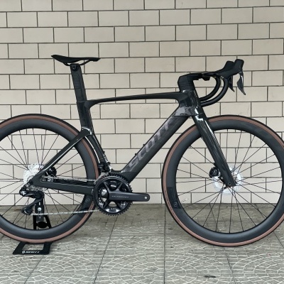 Bicicleta de estrada preta com pneus castanhos junto a parede de azulejos brancos
