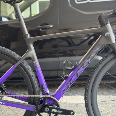 Bicicleta de estrada cinza e roxa com pneus pretos e selim preto, com texto SCOTT e DANI BIKES no quadro