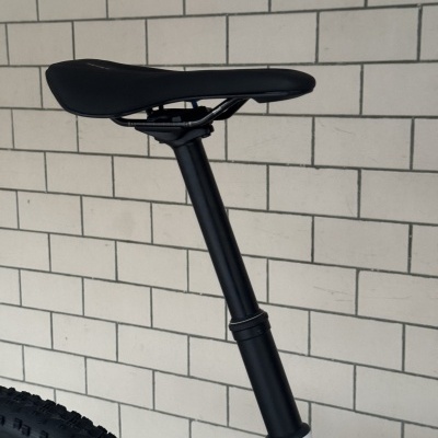 Selim de bicicleta preto e tubo de selim preto encostados numa parede de azulejos brancos
