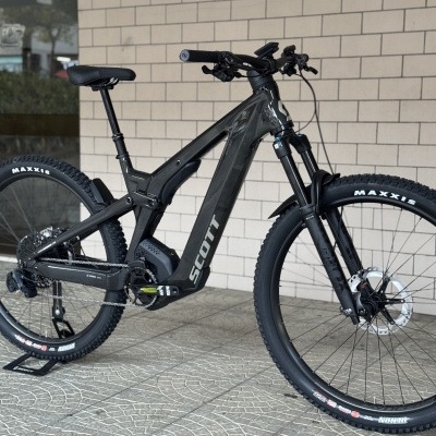 Bicicleta elétrica de montanha preta com pneus Maxxis e motor Bosch encostada numa parede.