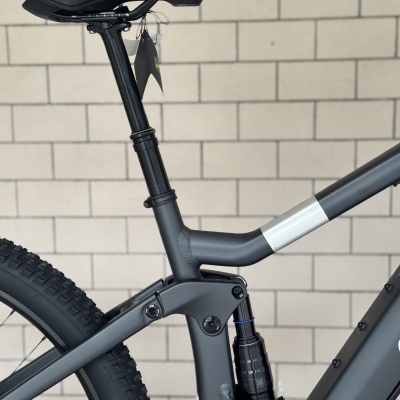 Parte traseira de bicicleta de montanha cinza com selim preto e suspensão, parede tijolos clara ao fundo.