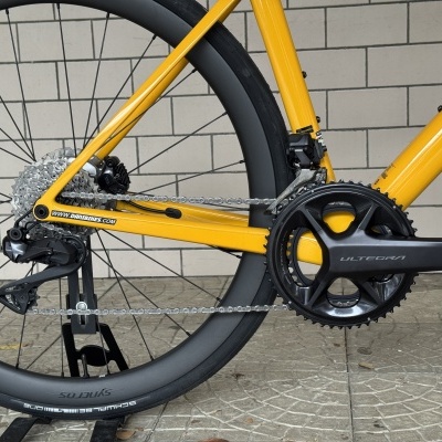Detalhe da roda traseira e pedaleira de uma bicicleta de estrada amarela com textos ULTEGRA e ADDICT RC
