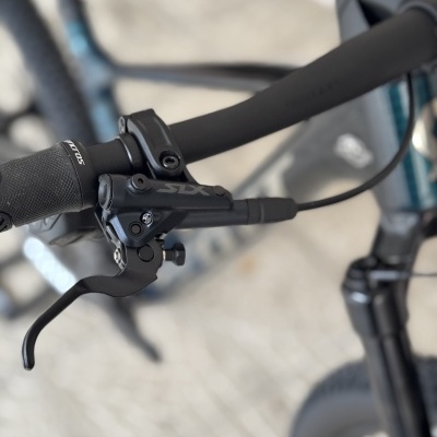 Punho e manete de travão de bicicleta preta com texto SDX, quadro e suspensão ao fundo.