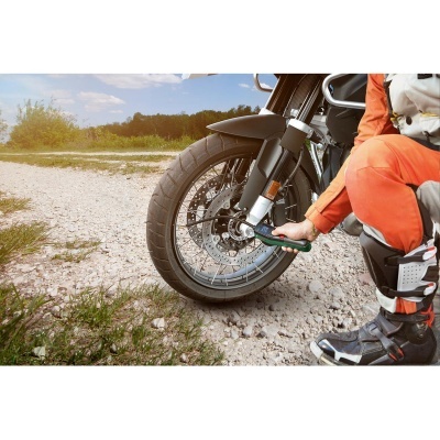 Motociclista com roupa laranja e preta a usar ferramenta na roda dianteira de mota preta em estrada de terra