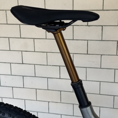 Selim de bicicleta preto com tubo dourado e estrutura cinzenta junto a parede de azulejos brancos