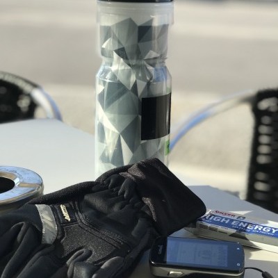 Garrafa de água desportiva, touca, barra energética e dispositivo eletrônico sobre mesa