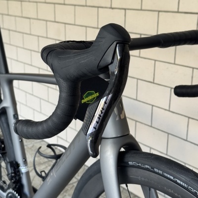 Bicicleta de estrada cinza com guiador em fita preta, punho de travão em carbono e pneu Schwalbe.