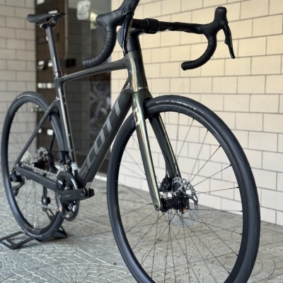 Bicicleta de estrada cinza escuro com pneus Schwalbe One e travões de disco contra parede de tijolos
