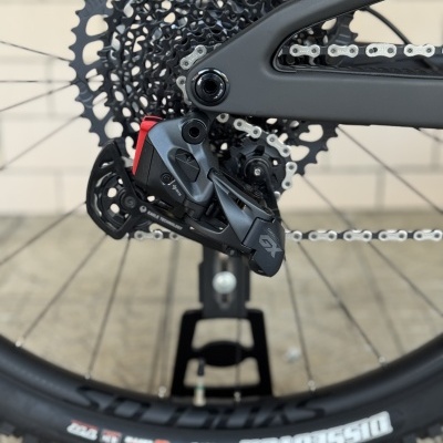Detalhe da roda traseira e transmissão de bicicleta preta com texto Sram GX e MAXXIS no pneu