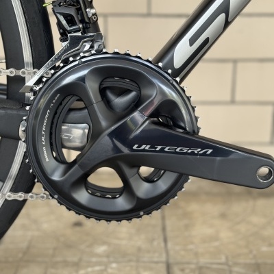 Peça de bicicleta preta com texto ULTEGRA e SHIMANO ULTEGRA 11S 50-34 MS em fundo de azulejos bege.