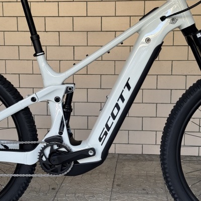 Bicicleta branca com quadro SCOTT e suspensão, contra parede de azulejos bege.